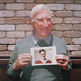 George Band holding a picture of himself when he was younger.