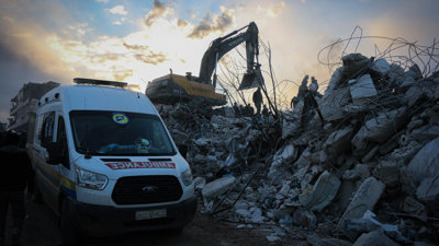An ambulance next to a destroyed building in a war zone.