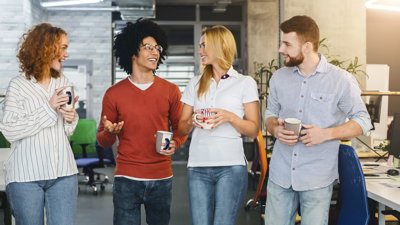 Two men and two women standing in office holding mugs and chatting