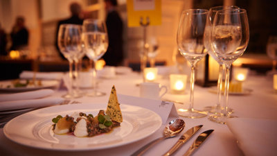 A formal dinner table with food, cutlery, wine glasses and glass candleholders with lit tealights.