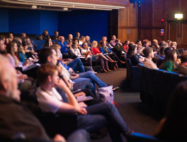 Large group of people sat in a lecture hall attending a presentation. 