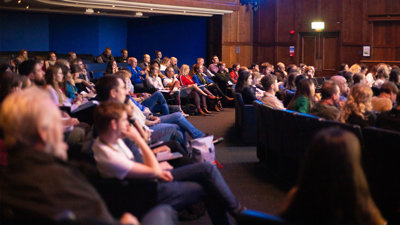 Large group of people sat in a lecture hall attending a presentation. 