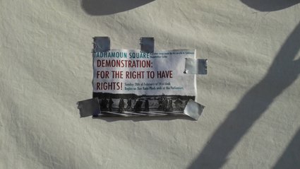 Flyer taped to a wall announcing a demonstration at Tadamoun Square with dates and location details.