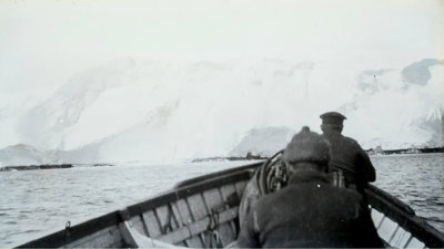 Old black and white photograph of two people in the front of a boat in Antarctica.