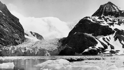 Black and white photograph showing a landscape with ice, snow and mountains.