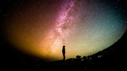 A silhouette of a person against a stary sky with bursting colours.