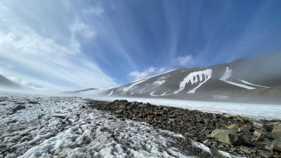 Low-angle shot of a windswept glacier with rocky surface and clear blue sky.