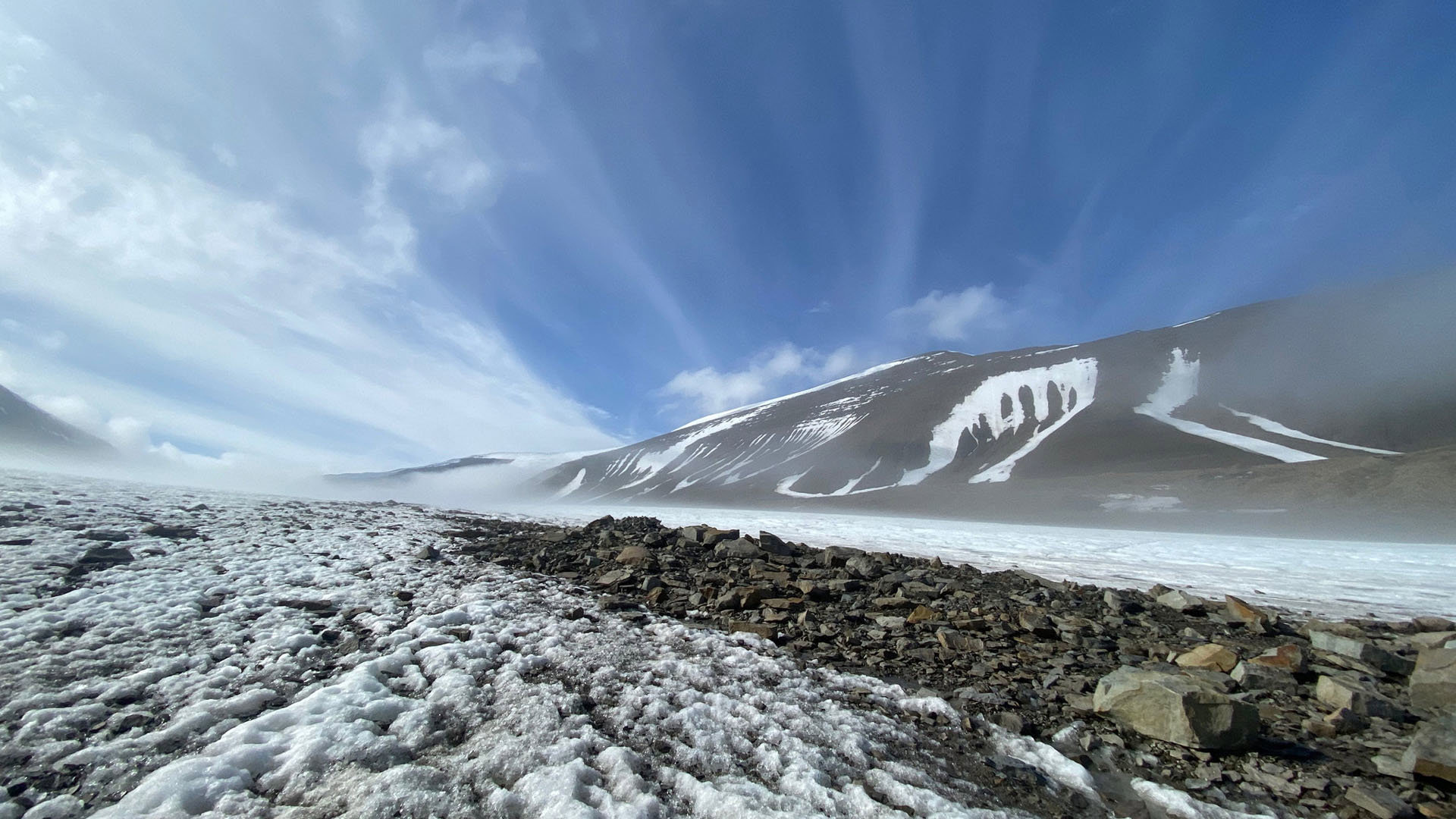 Low-angle shot of a windswept glacier with rocky surface and clear blue sky.