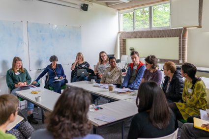 A group of twelve people sit around a table having a discussion.