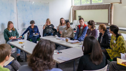 A group of twelve people sit around a table having a discussion. 