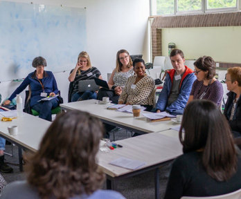 A group of twelve people sit around a table having a discussion. 