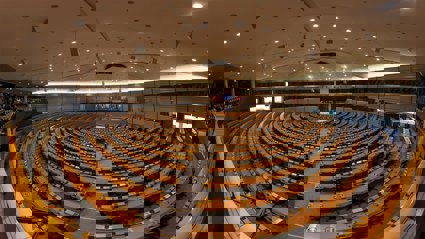 Circular rows of seats in a conference room with a stage at the front. There are European flags behind the stage.