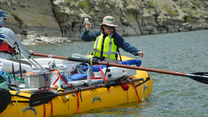 A person wearing a life jacket in a rubber boat taking measurements from a river.