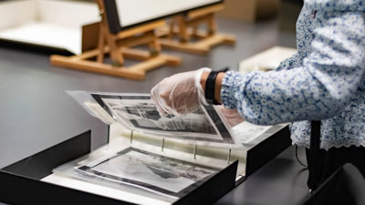 A researcher wearing archival gloves viewing historic photographs in a folder.