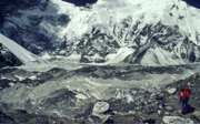 A man walking in a barren, rocky landscape with snowy mountains in the back.