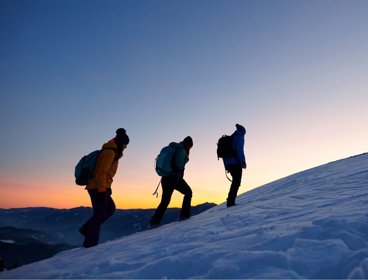 Three people hiking in snow against sunset backdrop.