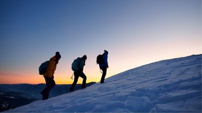 Three people hiking in snow against sunset backdrop.