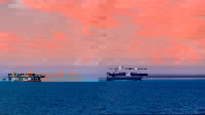 A cargo ship on the ocean with a pink sky