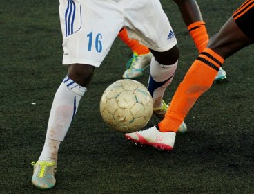 Close-up of two soccer players battling for the ball on an artificial turf pitch.