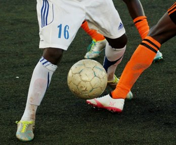 Close-up of two soccer players battling for the ball on an artificial turf pitch.