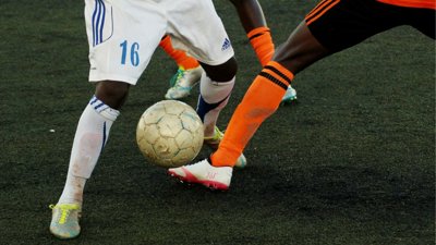 Close-up of two soccer players battling for the ball on an artificial turf pitch.