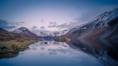A lake in foreground surrounded by snow-capped mountains.