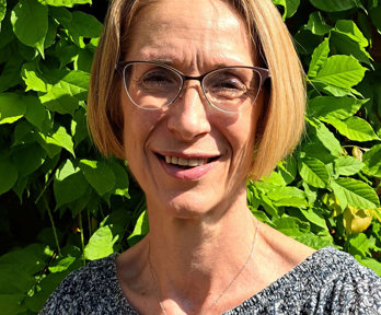 Headshot of Emma Espley posing in front of a hedge on a sunny day.