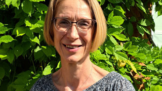 Headshot of Emma Espley posing in front of a hedge on a sunny day.