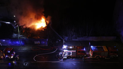 A fire burns at night with several fire engines nearby.