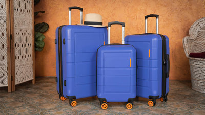 Three blue suitcases in a room with an orange wall.