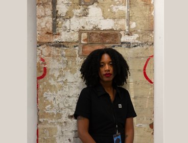 Person wearing a black polo shirt standing against a brick wall with red paint.