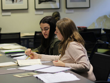 Two young people sat at a large table with papers and notebooks.