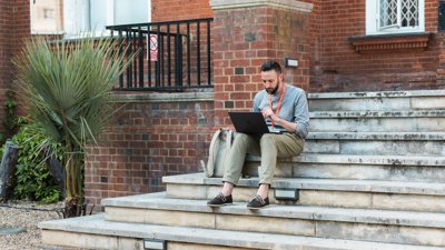 Person working on laptop on steps of the Royal Geographical Society.