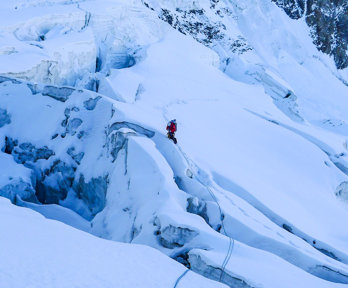 A mountain side covered in a thick layer of snow and ice, with in the distance a lone climber.