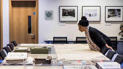 A person looking at historic materials, including maps, books, and photographs spread out on a large table.