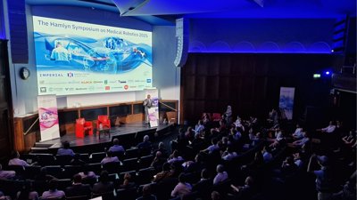 Audience and speaker in a lecture theatre. The words 'Hamlyn Symposium on Medical Robotics 2025' are projected on a screen.