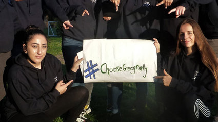 A group of students are holding and pointing at a sign that reads 'Choose Geography'.