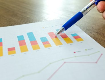 Person holding pen pointing at graphs on piece of paper. 