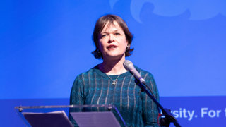 Professor Rachel Pain presenting on stage at a conference