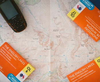 Closed Ordnance Survey maps titled English Lakes laying on top of an open map.