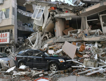 Cars in front of destroyed building post-earthquake.