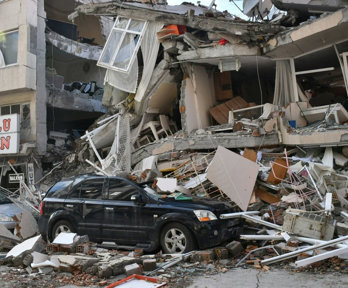 Cars in front of destroyed building post-earthquake.
