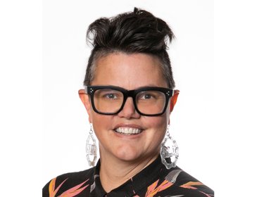 Person with dark hair wearing hoop earrings and a black top with orange and white patterns.