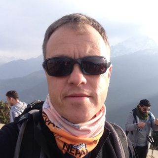Headshot of Carl Carter. He's outdoors, wearing sunglasses and a scarf that says Nepal.