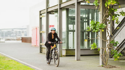 A businessperson in a suit wearing a bicycle helmet cycles past a modern glass building.
