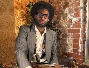 Profile image of a person holding an instrument in front of a brick wall