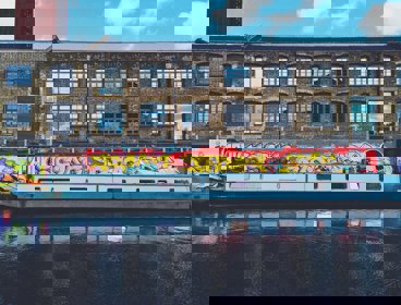 A canal boat with a background of an old industrial building and graffiti