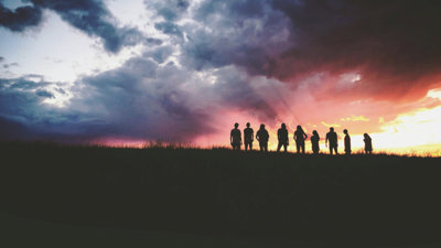 Silhouette of nine people standing on a hill against a sunrise.