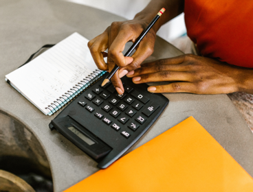 Close-up view of a person typing on calculator next to papers. 