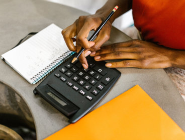 Close-up view of a person typing on calculator next to papers. 
